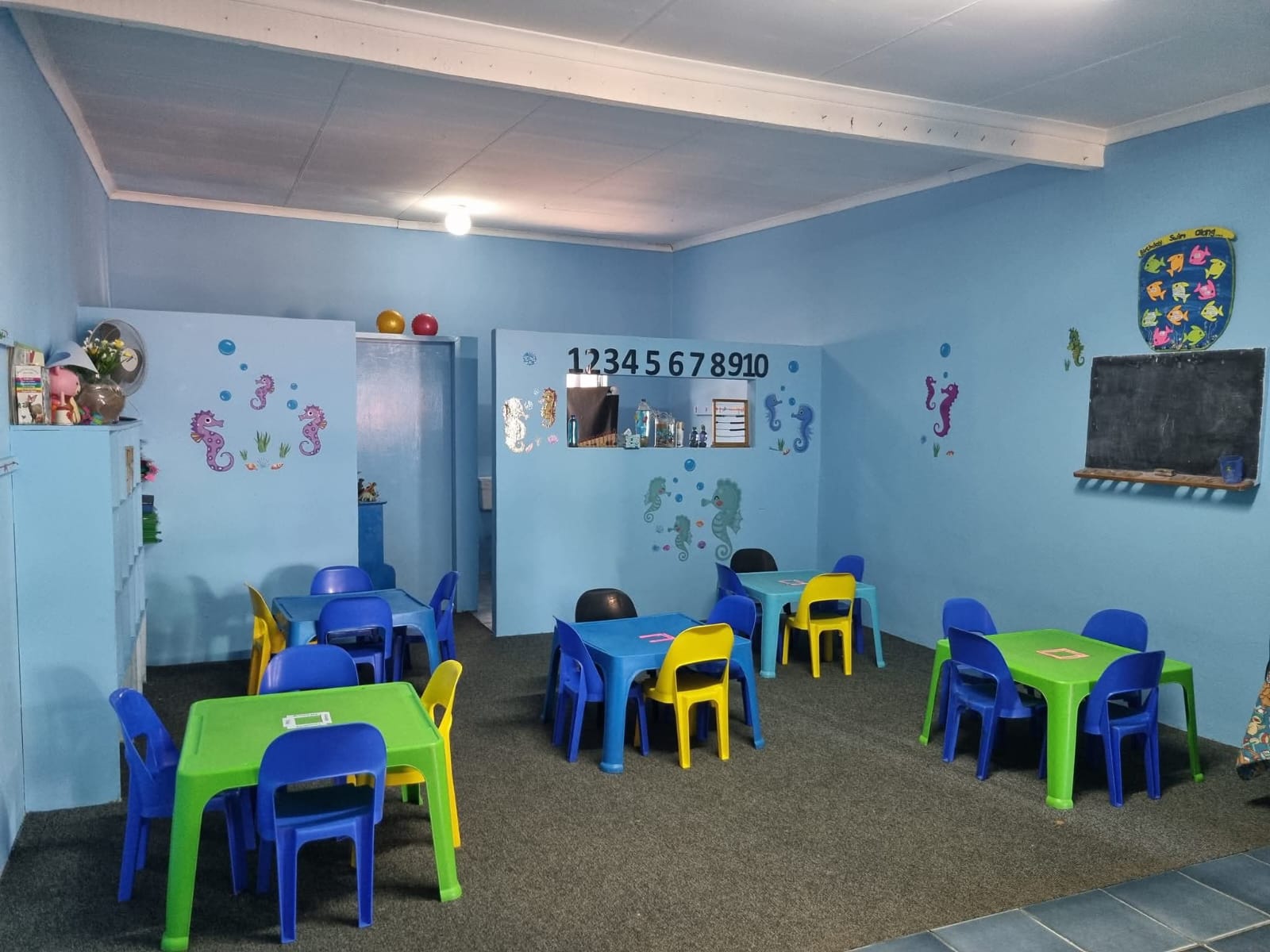 A bright blue classroom with child-sized tables and chairs